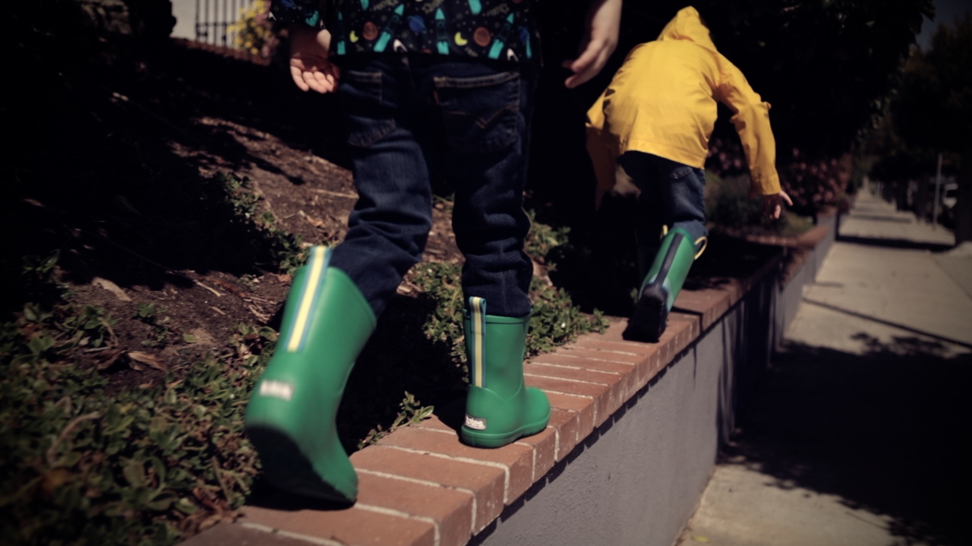 two boys walking on a wall in rubber boots